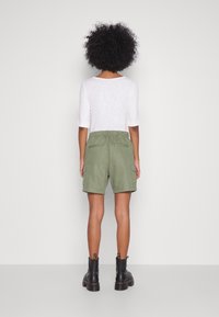 Pantaloni cargo verde oliva con vita elastica, tasche laterali e vestibilità comoda, abbinati a una maglietta bianca a maniche tre quarti e stivali neri.