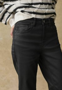 Melni denim džinsi ar klasisku piegriezumu, ar priekšējo pogu aizdari, sānu kabatām un gludu tekstūru. Pabeigti ar diskrētām šuvju detaļām.