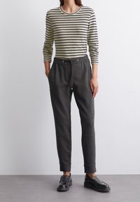 Camiseta de manga larga a rayas en verde y beige; pantalones joggers grises de ajuste relajado con cinturilla elástica, bolsillos con cremallera y puños acanalados; mocasines negros.