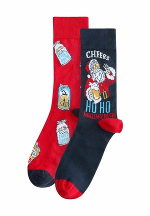 Rote und marineblaue Socken mit Feiertagsdesigns: Bierdosen auf der roten Socke und ein Weihnachtsmann mit Text auf der marineblauen Socke; aus einem Baumwollmix.
