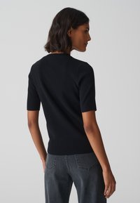 Zwart geribbelde gebreide top met korte mouwen en een getailleerd ontwerp. De achterkant toont een ronde hals en naadloze schouderdetails.