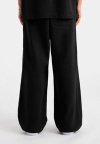 Zwarte, wijde sweatpants van een gladde stof, met een achterzak en afgeknipte zomen; gecombineerd met een zwarte, losvallende top.