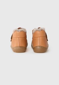 Botas de tobillo de cuero marrón con un suave forro de lana crema en el cuello. Suela de goma con un sutil branding. Acentos de costura distintivos en los laterales.