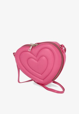 Sac bandoulière rose en forme de cœur avec des motifs de cœur matelassés, une fermeture éclair argentée et une sangle réglable sur fond blanc.