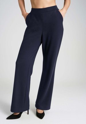 Pantaloni a gamba larga blu navy con una texture liscia, vita alta, tasche laterali e linee pulite, abbinati a eleganti tacchi neri a punta.