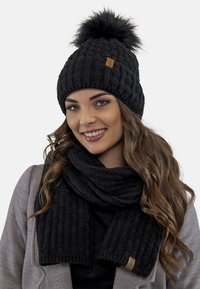 Sort strikket hue med en faux fur pom-pom og et matchende sort tørklæde med ribbet struktur. Indeholder et lille lædermærke.