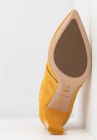 Chaussure pour femme à bout pointu en daim jaune avec semelle texturée et petit talon bloc, taille 37, vue de la semelle sur un fond blanc.