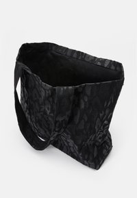 Zwarte tote bag met een textuur van luipaardprint, stevige stof en twee handvatten. De binnenkant is niet gevoerd en ruim.