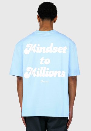 Light blue oversized t-shirt made of cotton, featuring white text on the back that reads "Mindset to Millions" with a subtle brand logo below.