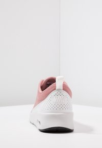 Zapatilla deportiva rosa con parte superior de malla y un talón blanco texturizado con perforaciones. Suela negra con una pestaña en el talón para facilitar el uso.