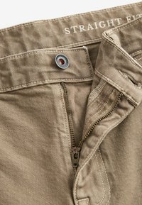 Pantalons droit en kaki avec une fermeture à bouton métallique, une braguette zippée et des poches avant plates. Tissu texturé avec de subtils motifs diagonaux.
