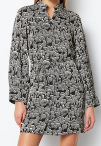 Schwarzes Kleid mit einem Blättermuster in Weiß und Grau. Verfügt über einen Kragen, lange Ärmel und eine taillierte Form mit einem gebundenen Gürtel. Seidene Textur.