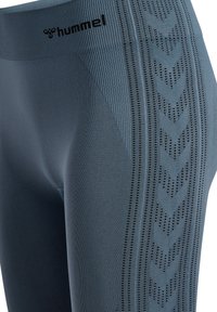 Eng anliegende Leggings in einem gedämpften Blauton mit strukturiertem Rippmaterial und einer gemusterten Seitenpartie, die Zickzack-Perforationen und ein schwarzes Logo aufweist.