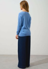 Helles blaues gestricktes Sweatshirt mit relaxed Fit, gerippten Bündchen und rundem Ausschnitt, kombiniert mit weit geschnittenen dunklen Jeans.