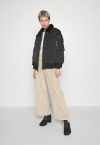 Sort bomberjakke med pelskrave, med lynlåslommer og lappe lommer, sat sammen med beige vidde bukser og sorte hælede støvler.