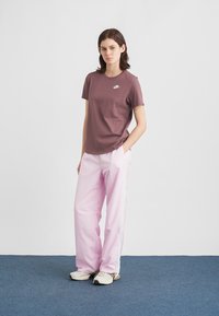 Μπορντό κοντομάνικη μπλούζα με μικρό λευκό λογότυπο, συνδυασμένη με ροζ ανοιχτόχρωμο παντελόνι παντελόνα με λευκές πλαϊνές ρίγες. Άσπρα αθλητικά παπούτσια.