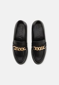 Black leather slip-on shoes featuring a gold chain accent on the front. Smooth texture with rounded toe and contrasting stitching detail.