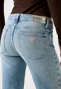 Jeans in denim azzurro chiaro a vita alta, con una tasca posteriore rettangolare e una toppa del logo triangolare rossa. Tessuto strutturato con dettagli di cuciture.