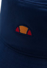 Granatowa czapka typu bucket z teksturowanej tkaniny. Posiada małe haftowane logo w kolorach czerwonym, żółtym i pomarańczowym z przodu.