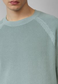 Helles blaues strukturiertes Strickpullover mit einem gerippten Rundhalsausschnitt und Raglanärmel, der subtile Nähte und einen weichen, atmungsaktiven Stoff aufweist.