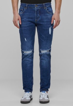 Jeans en denim bleu foncé avec des déchirures aux genoux, coupe régulière et léger effet de froissement. Dotés d'une taille classique et de cinq poches.