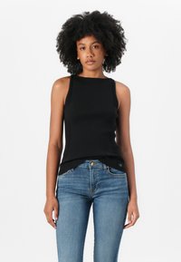 Black ribbed tank top with a sleeveless design and a crew neckline, paired with blue skinny jeans. Accentuated by subtle side slits.