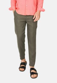 Pantaloni in lino verde oliva con una vestibilità slim e gambe affusolate, abbinati a sandali neri a due cinture. La camicia è color corallo, a maniche lunghe e dal taglio rilassato.