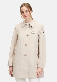 Hellbeige wasserdichter Mantel mit Kragen, drei großen Knöpfen und zwei seitlichen Taschen in einem schlichten, modernen Design.