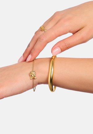 Goldener Armreif und Armband an einem Handgelenk; der Armreif ist glatt und abgerundet, das Armband zeigt ein Rosendesign mit funkelnden Details und einer Kette.