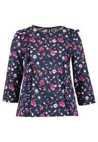 Granatowa bluzka z różowo-białym kwiatowym wzorem, rękawami o długości trzy czwarte, okrągłym dekoltem i z falbanami po bokach przodu.