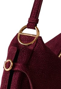 Burgundy textured fabric handbag with gold hardware accents, featuring a prominent round ring and a zipper closure.