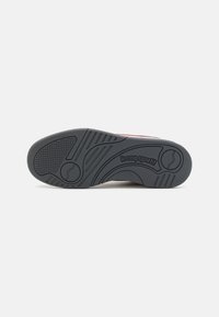 Suola di sneaker in gomma nera con motivi testurizzati e linee curve. Presenta un design circolare centrale e dettagli del marchio vicino al tallone.
