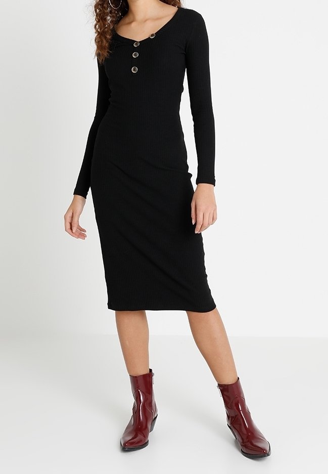 Černé žebrované šaty s dlouhým rukávem a výstřihem do véčka, zdobené třemi knoflíky na přední straně, v kombinaci s bordovými kotníkovými botami.