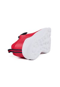 Baskets de sport rouges avec une tige texturée, semelle en caoutchouc blanche et un tirant noir rayé au talon. Matériau lisse et flexible.
