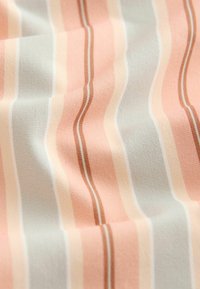 Tissu doux à rayures verticales dans des tons pastel pêche, beige et gris clair, présentant de légers plis et des détails de texture.