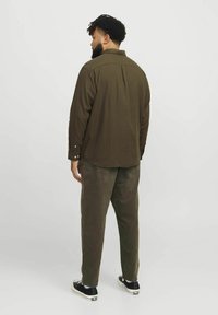 Olive green casual shirt with buttoned cuffs, paired with matching pants. Features a straight cut and back pleat design. Black sneakers.