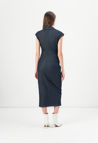 Dongerik midi-kjole med korte cap sleeves, tettsittende liv og utskriftet skjørt. Mørkeblå stoff med subtile sømdetaljer.