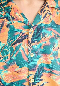 Short-sleeve button-up shirt in teal, orange, and pink with abstract floral patterns; features a collar and four light-colored buttons.