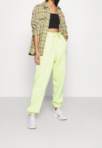 Grön rutig skjorta över en svart croppad topp, tillsammans med lösa, ljusgröna sweatpants med elastisk midja och manschetter.