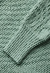 Pletený svetr s texturovaným povrchem ve světle zelené barvě. Žebrované manžety přidávají na detailech; látka vypadá měkce a teple, vhodná pro chladnější počasí.