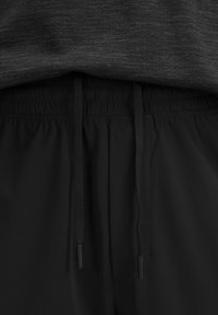 Schwarze Shorts mit elastischem Bund, ausgestattet mit Kordeln und einer glatten Textur, kombiniert mit einem dunkelgrauen Oberteil, das ein meliertes Muster zeigt.