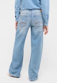 Šviesiai mėlynos plačios kojos džinsai su šiek tiek nusiskinusia apdaila. Turėtų dvi užpakalines kišenes su išskirtiniu siuvinėjimu. Džinsinis audinys, laisvas pritaikymas.