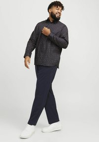 Une chemise à motifs sombres avec de petits motifs floraux, associée à un pantalon rayé bleu marine et des baskets blanches. Tenue décontractée présentée.
