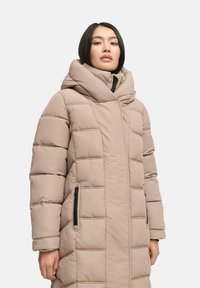 Beige gewatteerde jas met een hoge kraag, gequilt ontwerp, ritszakken en een gladde textuur. Heeft lange mouwen en een A-lijn vorm.