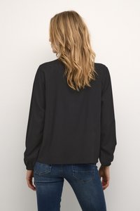 Μαύρη μπλούζα μακρύ μανίκι με άνετη εφαρμογή, στρογγυλή λαιμόκοψη και ρεβέρ με συγκεντρωμένες ραφές, συνδυασμένη με μπλε τζιν. Λείος υφασμάτινος σχεδιασμός με ελάχιστες λεπτομέρειες.