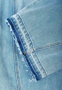 Light blue denim jeans close-up showing frayed, distressed hem and detailed stitching along the edge.