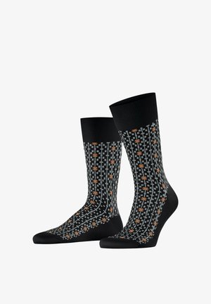Chaussettes noires à bord côtelé avec un motif à carreaux gris et de petits dessins d'astérisques orange répartis sur toute la surface.