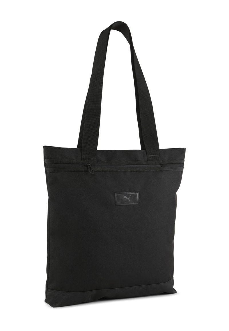Sac fourre-tout noir en tissu durable. Doté de deux poignées, d'une fermeture zippée sur le dessus et d'un petit écusson logo à l'avant.