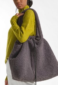 Borsa tote in tessuto morbido grigio con forma arrotondata, ampia apertura e chiusura con coulisse. Dettaglio con cordino bianco e nero.