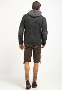 Gebreide cardigan in donkergrijs met een gestructureerd patroon, voorzien van een capuchon, elleboogpatches en gecombineerd met een bruine short en kniekousen.